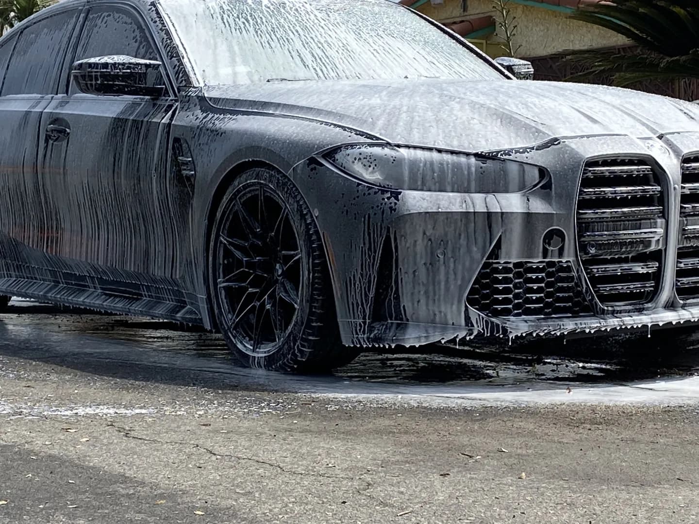 Black BMW covered in thick wash foam during an exterior wash