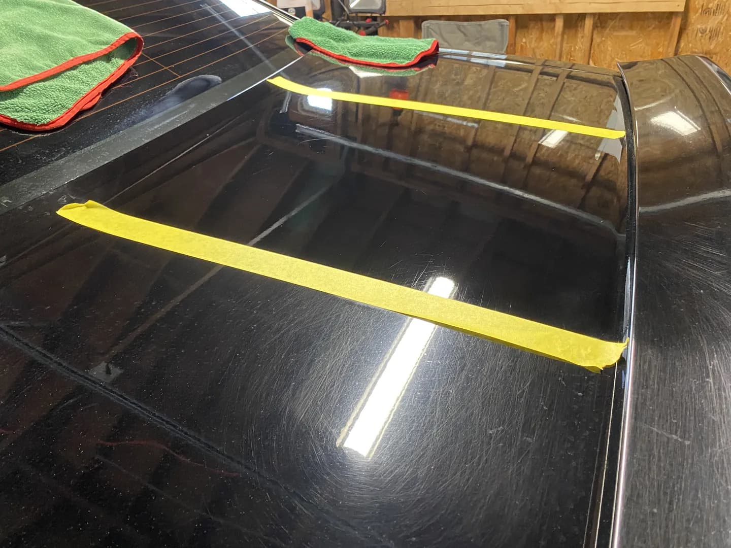 Tape line on black paint mid-correction, the polished side showing deeper gloss